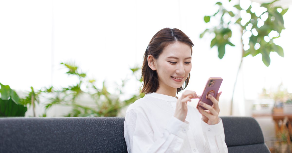 観葉植物のある部屋のソファでスマホを操作する女性