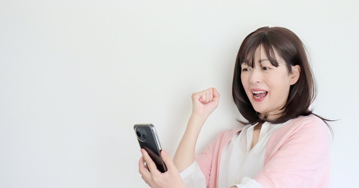 スマホの画面を見て、笑顔でガッツポーズをする女性