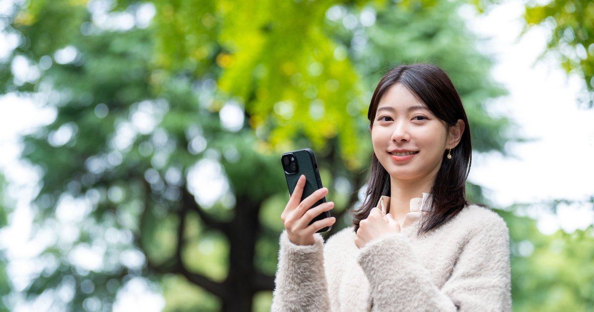 木々のある屋外でスマホを手に立つ女性