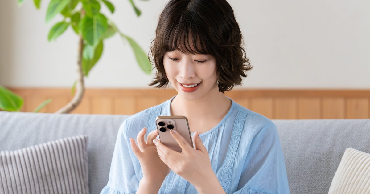 ソファに座り、スマホの画面を見ながら指で操作する女性