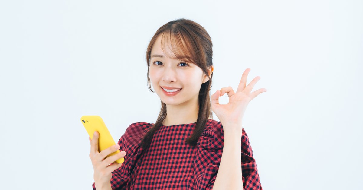 黄色いスマホを手に、指でOKサインをする女性