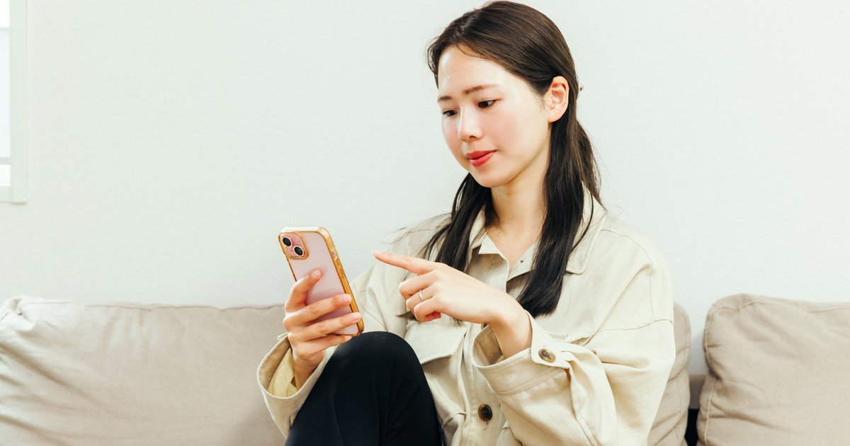 ソファに座り、スマホの画面を指差す女性