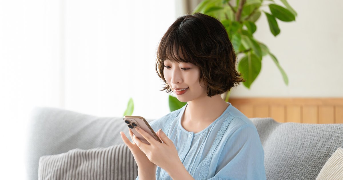 ソファに座り、両手で持ったスマホの画面を確かめる女性