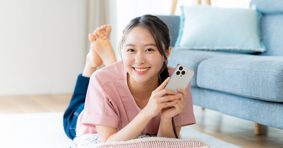 床に寝そべってスマホを持ち、笑顔でくつろぐ女性