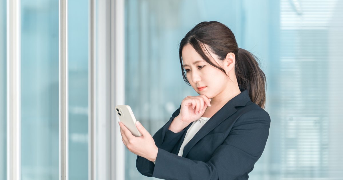 窓辺に立ち、スマホの画面を確かめる女性