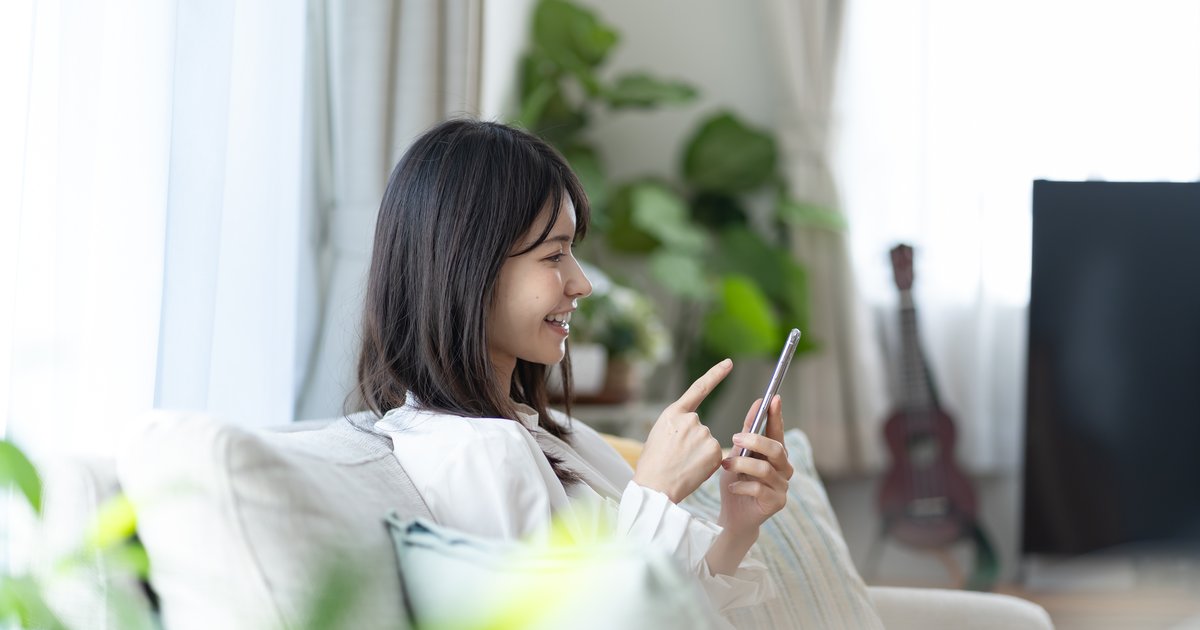 ソファに座り、スマホの画面を指差して操作する女性