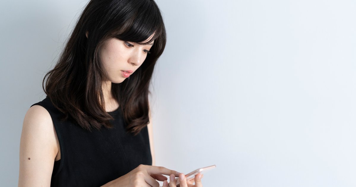 白い壁の前で、手元のスマホをじっと見る女性