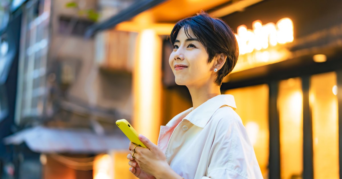 夕暮れの街角でスマホを手に立つ女性