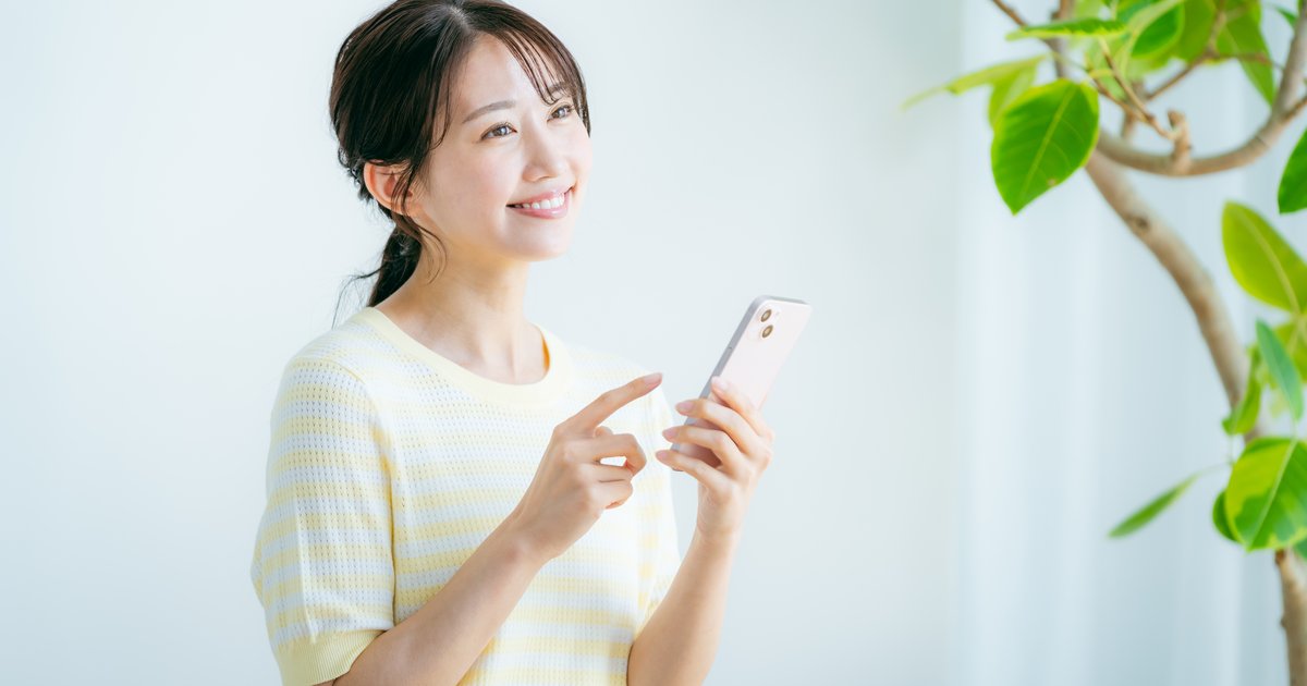 スマホを指差しながら笑顔で立つ女性