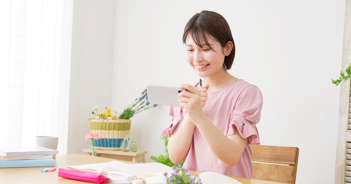 机にノートを広げ、スマホを手に持つ女性