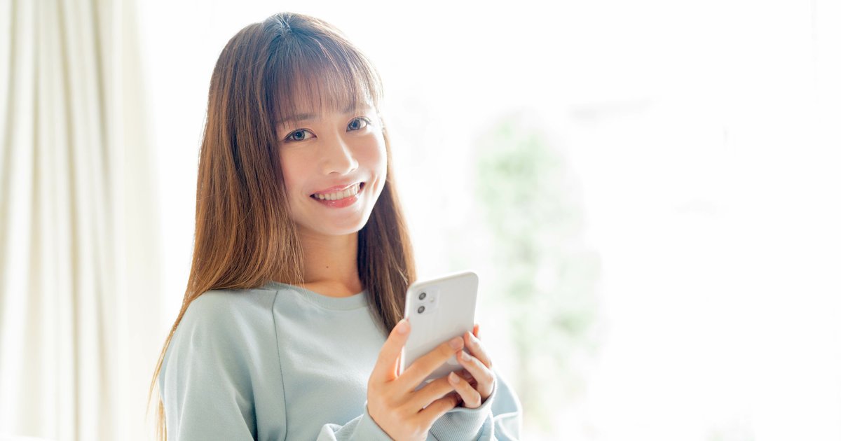 窓辺でスマホを手に持ち笑顔の女性