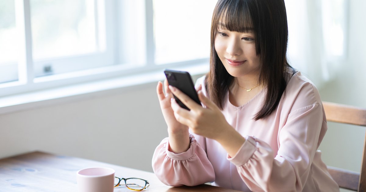 木のテーブルでスマホの画面をじっと見る女性