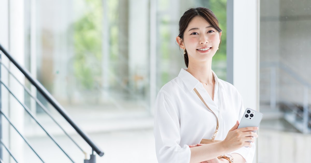 明るい建物の中でスマホを手に立つ女性