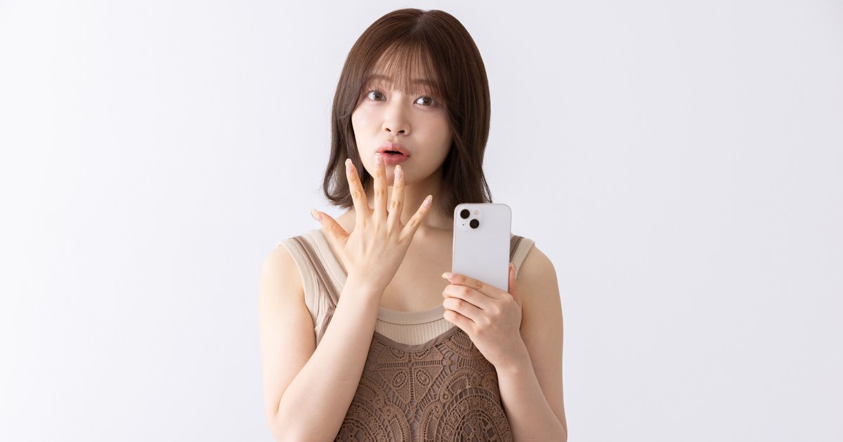 スマホを持ち、口元に手を当てて驚いた表情の女性