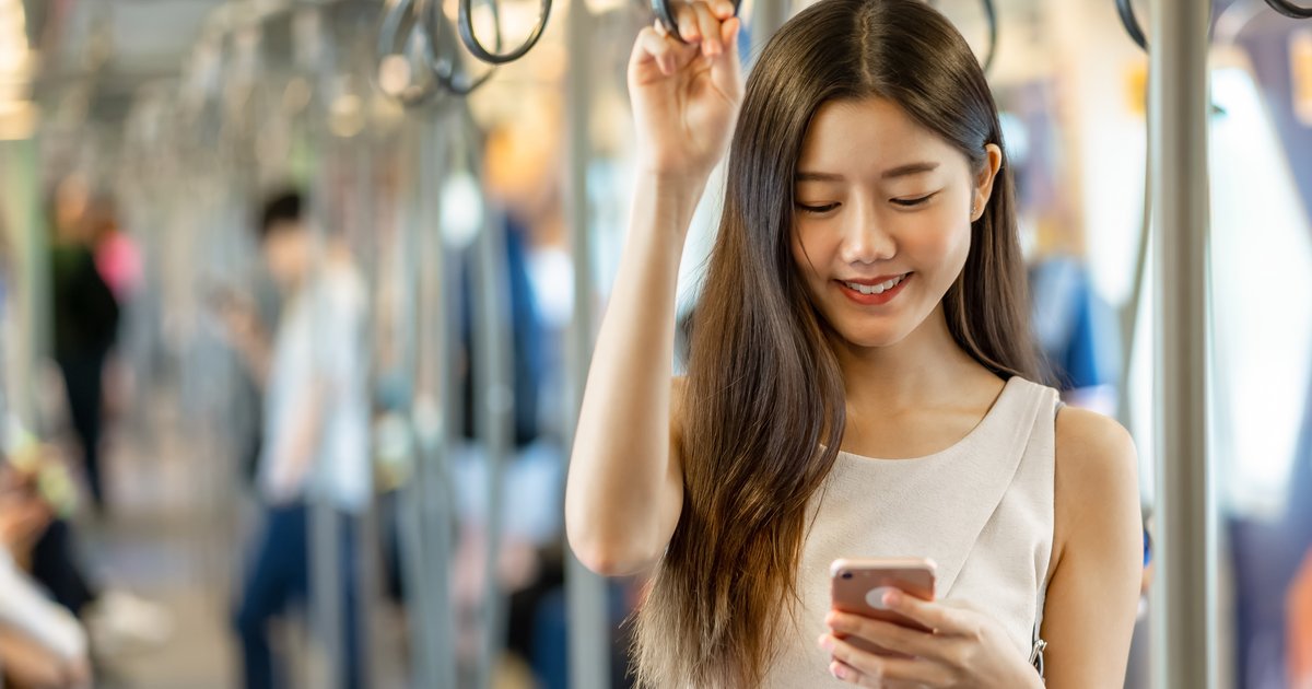 電車の中で立ったまま、スマホを見て微笑む女性
