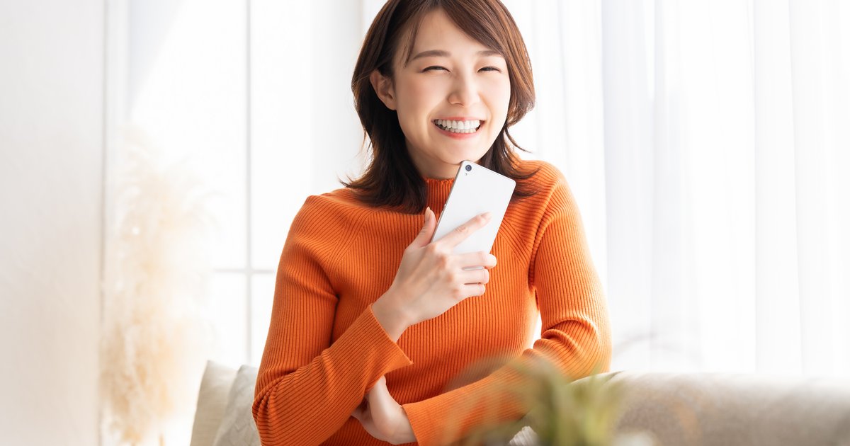 スマホを胸元に持ち、明るい部屋で笑う女性