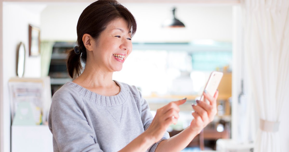 自宅の台所でスマホを操作して笑う女性