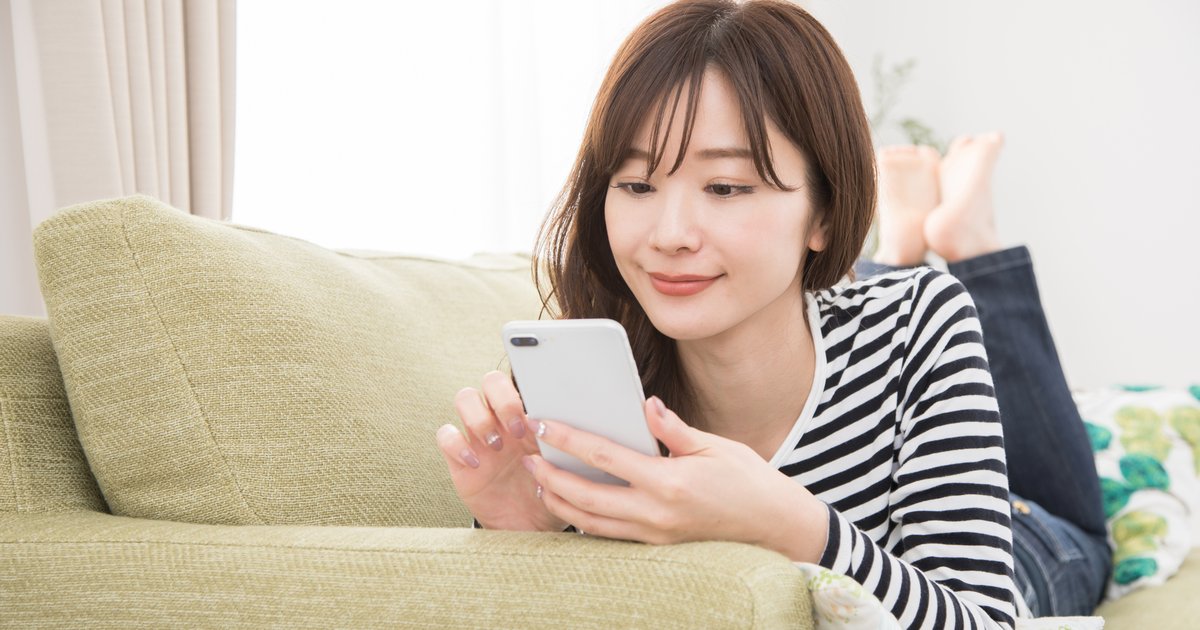 ソファでくつろぎながらスマホの画面を見る女性